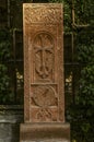 Red tuff khachkar with an arch carved with a cross, a figure of a Saint and a round symbol of eternity on the alley of stone cross