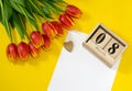 Red tulip flowers near cubic wooden calendar with date of 8 March, wooden heart and sheet of white paper with coopy space. Royalty Free Stock Photo