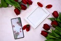 Red tulips bouquet, phone and white photo frame on pink background= Royalty Free Stock Photo