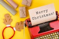 red typewriter with the text & x22;Merry Christmas!& x22;, gift boxes and wrapping paper on yellow background