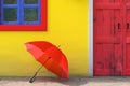 Red Umbrella in front of Retro Vintage European House Building with Yellow Wall, Red Door and Blue Windows, Narrow Street Scene.