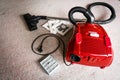 A red vacum cleaner with old and new vacum dust bags and hepa filter laying on a white carpet floor.