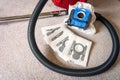 A red vacum cleaner with old and new vacum dust bags and hepa filter laying on a white carpet floor.