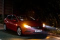 The red Vauxhall Astra car waiting on the side of the road in the night rain waiting for a help with flashing warning lights