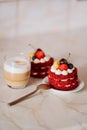 Red velvet cakes, portioned, decorated with cherries and strawberries. transparent mug of cappuccino with a cinnamon stick. delici Royalty Free Stock Photo