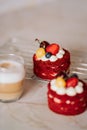 Red velvet cakes, portioned, decorated with cherries and strawberries. transparent mug of cappuccino with a cinnamon stick. delici Royalty Free Stock Photo