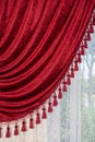 A red velvet curtain decorated with tassels hangs on the window