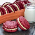 Red velvet sandwich cookies with cream cheese filling on wooden table, square format