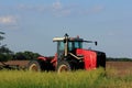 A Red Versatile Tractor in a farm field with blue sky and clouds