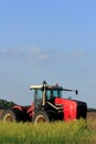 A Red Versatile Tractor in a farm field with blue sky and clouds