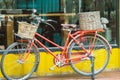 Red vintage bicycle with rattan baskets parked near yellow wall