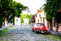 Red vintage car in cobbled street during sunset, trees