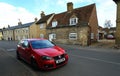 Red Volkswagen Golf Motor car parked in front of historic cottage.