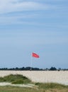 Red Warning Flag Flying High on a Coastal Beach Under Blue Sky Royalty Free Stock Photo