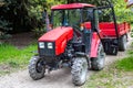 Red wheeled tractor with a trailer on a dirt road in a forest Royalty Free Stock Photo