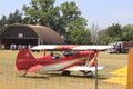 A Red and White Airplane at a Flying Farmers show sitting by the runway by the airplane hanger on a colorful day.