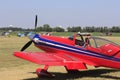 A Red and White Airplane at a Flying Farmers show sitting by the runway by the airplane hanger on a colorful day.