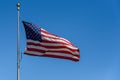 Red, white, and blue of an American flag flying in a breeze against a bright blue sky Royalty Free Stock Photo