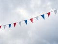 Red, white and blue festive bunting flags against sky background. Triangle shapes against cloudy sky. Royalty Free Stock Photo