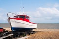 Red, white and blue wooden fishing boat, moored on a pebble beach on a bright summer day Royalty Free Stock Photo