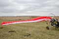 Red and white canopy paraglider lying on green grass against cloudy sky background Royalty Free Stock Photo