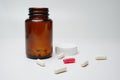 Red & white Capsule pills in front of brown bottles on white background.