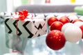 Red and white Christmas balls are scattered on the glass table. Christmas gift, wrapping paper, red bow. New Year, xmas Royalty Free Stock Photo