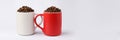 Two coffee mugs filled with coffee beans on light background