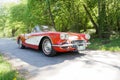 Red and white color Chevrolet Corvette classic car from 1958 driving on a country road