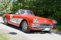 Red and white color Chevrolet Corvette classic car from 1958 driving on a country road