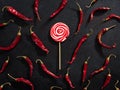 Red and white colored swirl round candy lollipop with dry red hot chili peppers. Sweet and hot food contrast Royalty Free Stock Photo