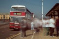 Red and White double decker Leyland Olympian preserved bus at bus stop. Ghostly blurred passengers wait to board and travel