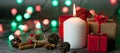 Red and white festive candles burn with a yellow flame on a table among gifts in craft paper, rattan balls, cinnamon sticks and