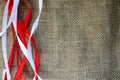 Red and white festive ribbons, threads against the texture of brown old linen cloth, linen natural material with a coarse perpendi