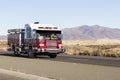 Red and white fire truck driving down a road in the desert responding to an emergency call