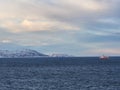 Norwegian red and white fishing boat in fjord near snowy mountains Royalty Free Stock Photo