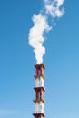 Red and white industrial chimney with a cloud of white smoke against blue clear sky.