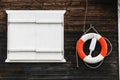 Red and white lifebuoy lifebelt with ropes hanging from a dark brown painted wooden wall