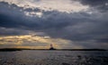 A red and white lighthouse on an island surrounded by storm clouds