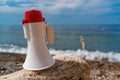 Red and White loudspeaker or horn megaphone for important public information against blue sea at beach.