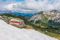 Red and white marking of the hiking trail in the Austrian Alps. Sunny mountain panorama with snow in the foreground.