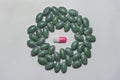 Medicine capsule surrounded by green oval pills on a white background