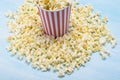 A red-white paper cup filled with popcorn stands in corn kernels Royalty Free Stock Photo