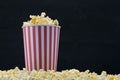 Red-white paper cup filled with popcorn stands in grains of corn, on a dark background Royalty Free Stock Photo