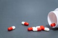 Red and white pill capsules poured from a white plastic bottle container. Global healthcare concept on gray background Royalty Free Stock Photo