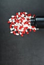 Red and white pills with capsules spilled out of a black jar on a black background. Royalty Free Stock Photo