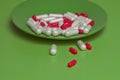 Red and white pills closeup spill out of a green plate on a green background. Royalty Free Stock Photo