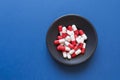 Red and white pills lie on a black plate. Dark blue background.