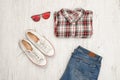 Red and white plaid shirt, glasses, sneakers and jeans. Wooden background. Fashionable concept, top view