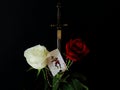 Red and white roses, metal stiletto replica and card with jester on black background. Symbolic concept Ã¢â¬â life, chance, change